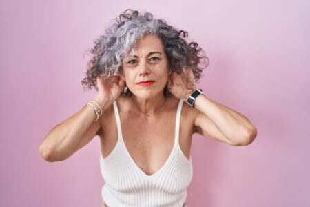 Cabelo cacheado branco: sua beleza natural em evidência Mulher com os cabelos grisalhos, com o fundo da imagem rosado.