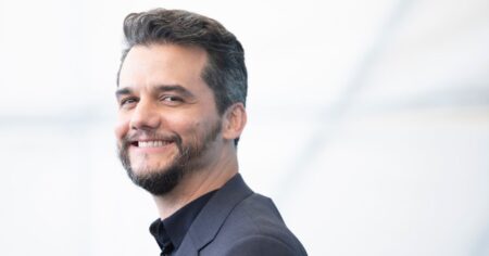 Wagner Moura pede dica a Bruna Marquezine ao ir a desfile da Chanel pela 1ª vez; veja Wagner Moura sorri durante pose oficial em evento, usando terno escuro.