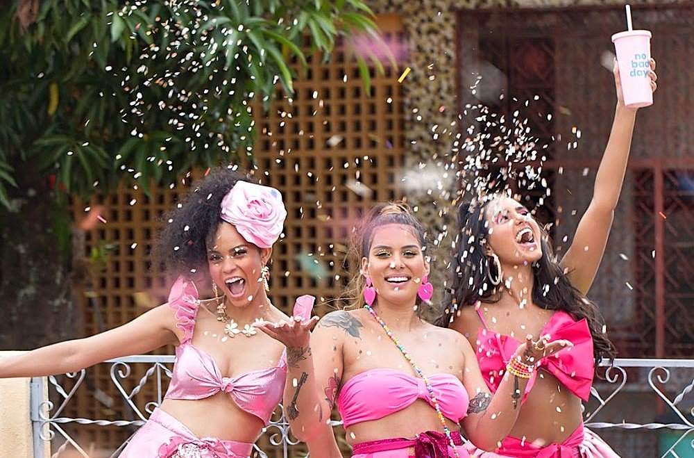 Mulheres fantasiadas e comemorando com confetes durante o Carnaval 2026, usando looks vibrantes e acessórios festivos em um bloco de rua.