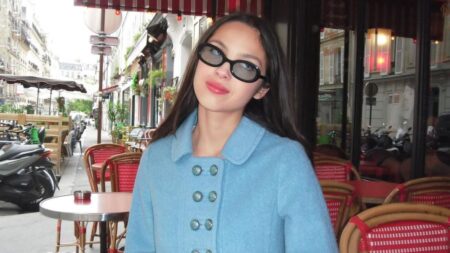 Olivia Rodrigo posa usando óculos escuros e casaco azul em café de rua